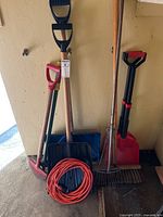 Group of shovels, rake, broom, pick mattock and cord against wall