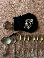 Group shot of all sterling items: chain on pouch, napkin ring, caddy spoon, six matching teaspoons, commemorative teaspoon