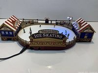 Full view of oval rink showing buildings, fencing, sign, skater figures and power cord attached