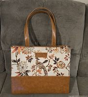 Front view of canvas and leather floral tote handbag showing pattern, leather bottom, and handles