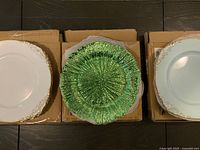 Group of charger plates: white with gold and green variants stacked on boxes