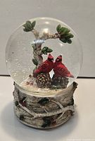 Full view of snow globe showing cardinals, tree, faux snow and birch-style base