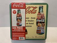 Front of sealed metal tin with Coca-Cola graphics and 500-piece puzzle sleeve visible