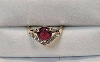 Front view of gold-tone ring showing red central stone and V-shaped rhinestone accents