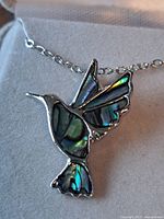 Close-up of hummingbird pendant showing abalone inlay and silver-tone finish