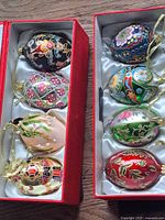 Two red silk-lined boxes each holding four decorated egg ornaments