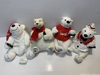 Front view of four Coca-Cola polar bear plush toys showing size, outfits and condition