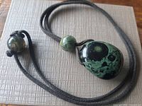 Front view of nebula stone pendant necklace showing green orbicular pattern and suede cord