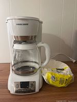 Front view of Black+Decker white drip coffee maker with glass carafe and bag of filters