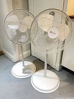 Two white Utilitech pedestal fans standing side by side