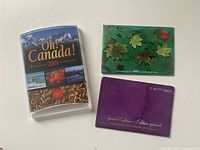Front view of three sealed coin sets: 2001 Oh Canada! plastic case, 2003 green standard set envelope, 2003 purple special edition envelope