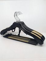 Stacked set of six black wooden hangers with metal hooks and beige rubber strips