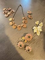 All three jewelry sets laid out: copper necklace, bracelet, earrings; white leaf brooch & earrings; pink flower brooch & earrings