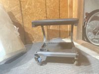 Front view of rolling mechanic seat showing frame, casters, tray