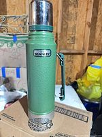 Full view of green Stanley thermos with cup lid and handle