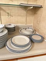 Stacked assorted dinner and salad plates, bowls visible on countertop
