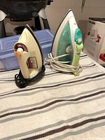 Two electric irons side by side on striped towel