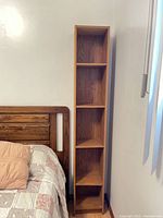 Full view of tall narrow brown MDF shelving next to bed