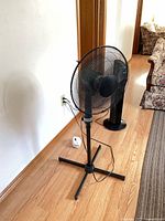 Full view of black pedestal fan on wooden floor