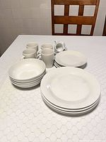 Dinnerware pieces grouped on table: mugs, bowls, plates, saucer