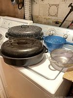 Two graniteware roasters, blue plastic colander, stainless mesh strainer on washer top