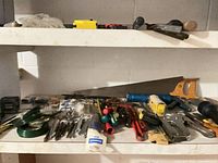 Shelf with various hand tools including saw, staple gun, screwdrivers, blades and wire