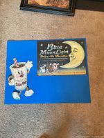 Both metal signs displayed on carpet: soda pop sign and Blue Moon Light Drive-In Theatre sign