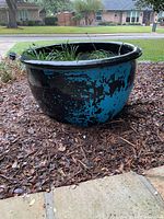 Front view of large black planter with distressed teal finish set on mulch