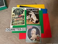 Four vintage tobacco advertising metal signs laid out on coloured boards