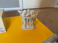 Front view of Mikasa three-angel porcelain figurine on yellow surface, box partially visible