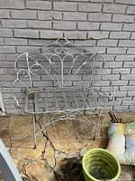 Front view of metal garden bench showing scroll back and slatted seat, paint wear visible