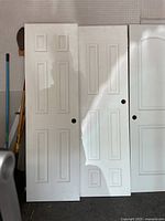 Three white interior slab doors standing vertically showing panel styles and bore holes