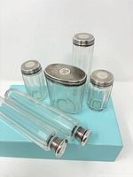 Six clear fluted glass containers with sterling lids displayed on box