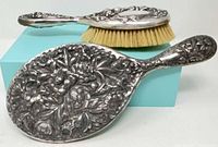Mirror and brush showing ornate floral silver-plated backs