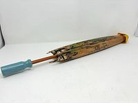 Closed parasol showing light blue handle, wooden shaft, damaged rib tips