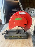 Full view of red chop saw on black base showing vise and wheel guard