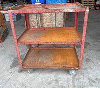 Front view of red metal 3-shelf tool cart showing rust and casters