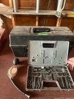 Tap and die set open in front of black plastic toolbox with antifreeze tester to side