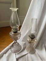 Two pressed glass oil lanterns side by side with chimneys installed