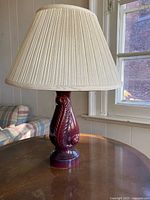 Front view of burgundy ceramic lamp with feather motif and pleated shade