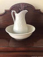 Pitcher resting in basin on wooden dresser, full view