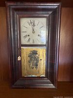 Full front view of clock showing wood case, dial and lower painted glass