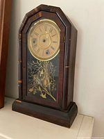 Front view of mantle clock, showing dial and glass with bird motif