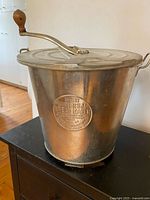 Front view showing bucket shape, lid, crank handle and wooden knob