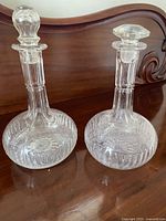 Both glass decanters with stoppers displayed side by side