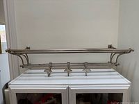 Front view of metal wall-mounted towel rack showing top shelf and lower bar with hooks