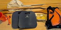 All items laid out: two paddles, life jacket, knee pads, bailer bucket, flashlight, Pelican case, insect net