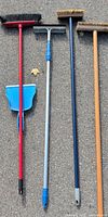 Full view of four long-handled tools and dustpan laid on pavement