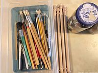 Plastic tub with assorted paintbrushes and pencils, wooden rods, glass jar of buttons