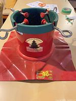 Front view of red and green Santa’s Solution metal Christmas tree stand showing logo decal, water reservoir and bolts